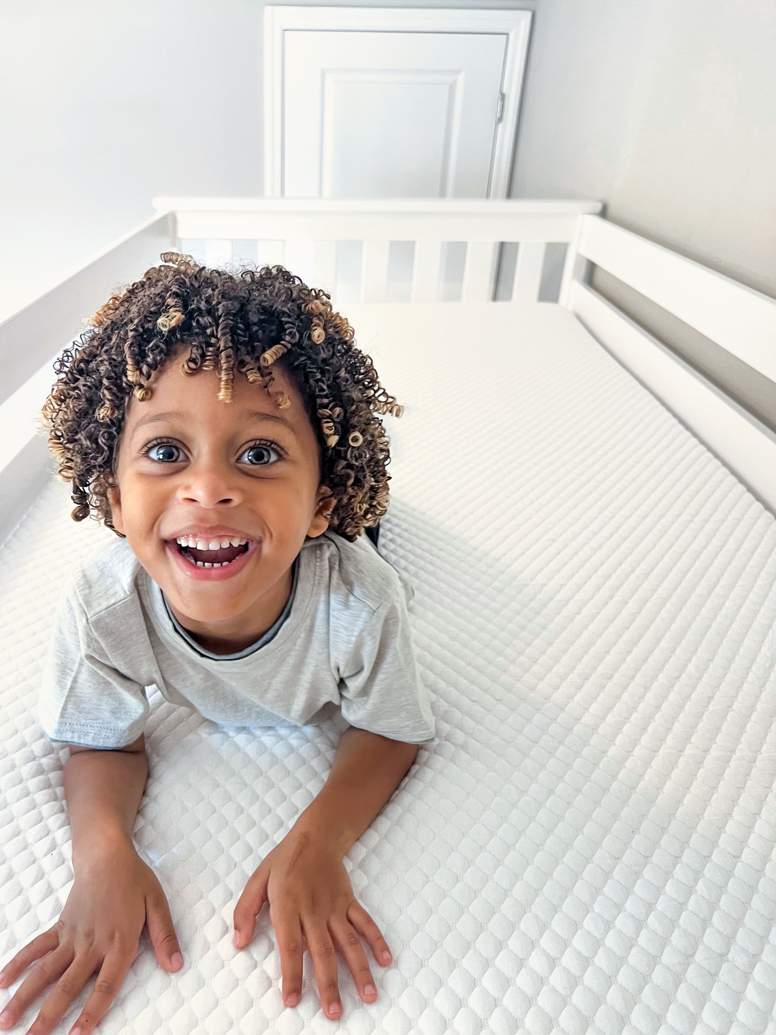 Little boy smiling and laying on a clean, white mattress.