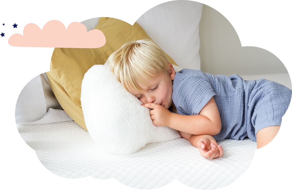A young boy dressed in blue, lying with his head on a fluffy white pillow, sucking his thumb while he sleeps.