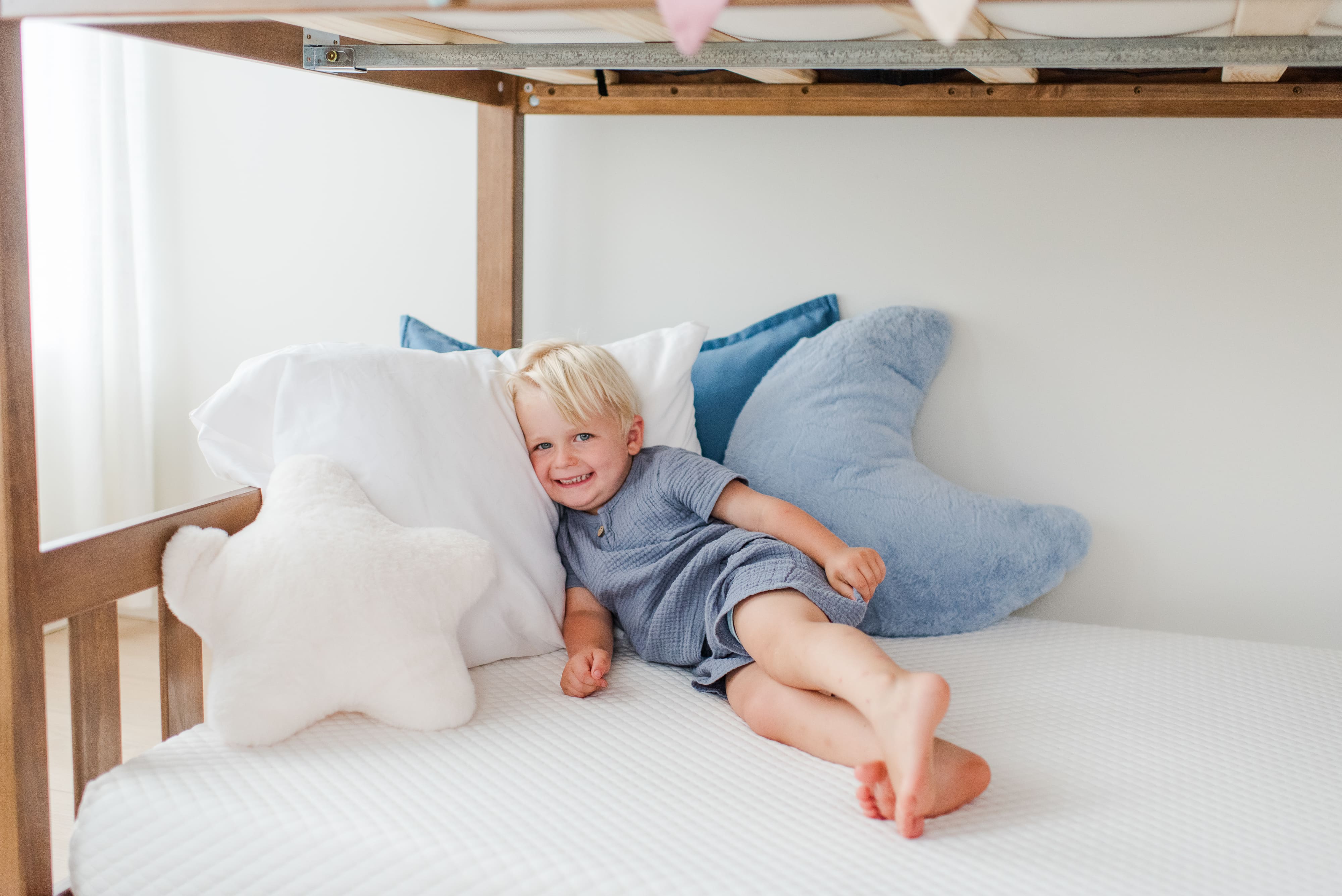 Child sitting on a bed with star-shaped pillows and a white blanket.