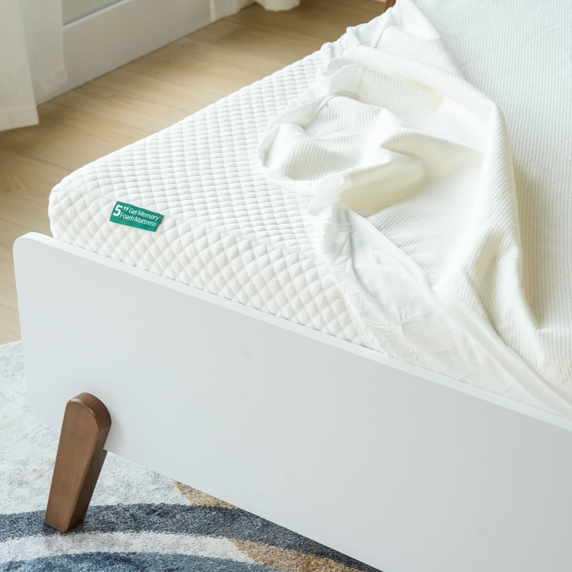 Close-up of a bed with a white quilted memory foam mattress and a rumpled white sheet.