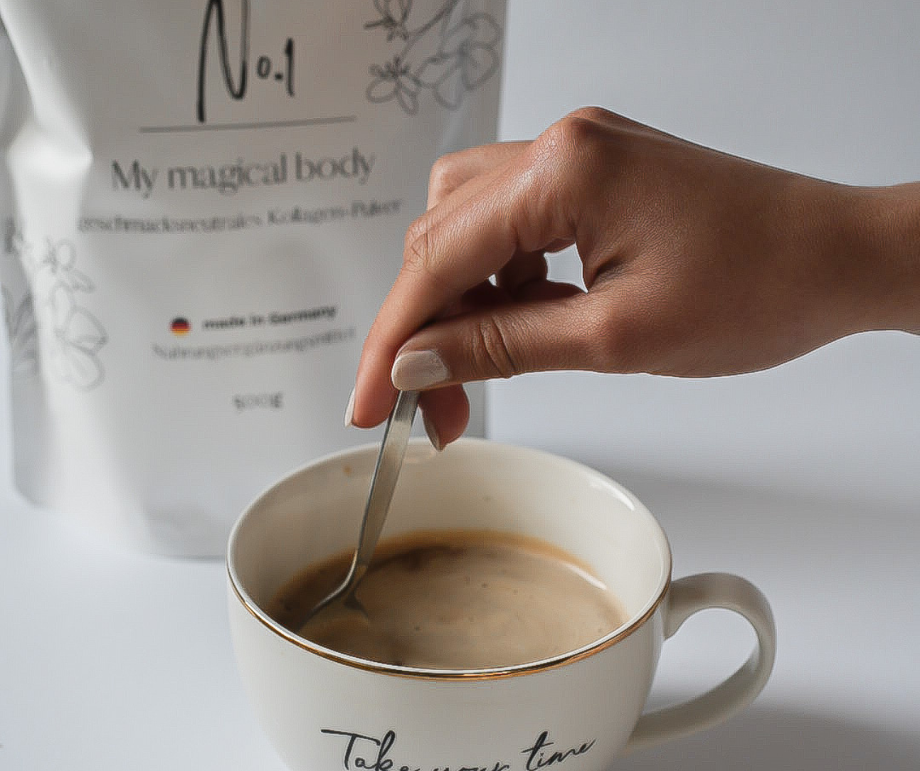 Hand stirring a cup of coffee with a spoon, next to a product package.