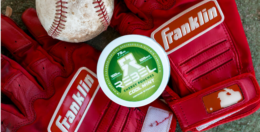 Red baseball gloves, a baseball, and a green Rebel energy pouches container.