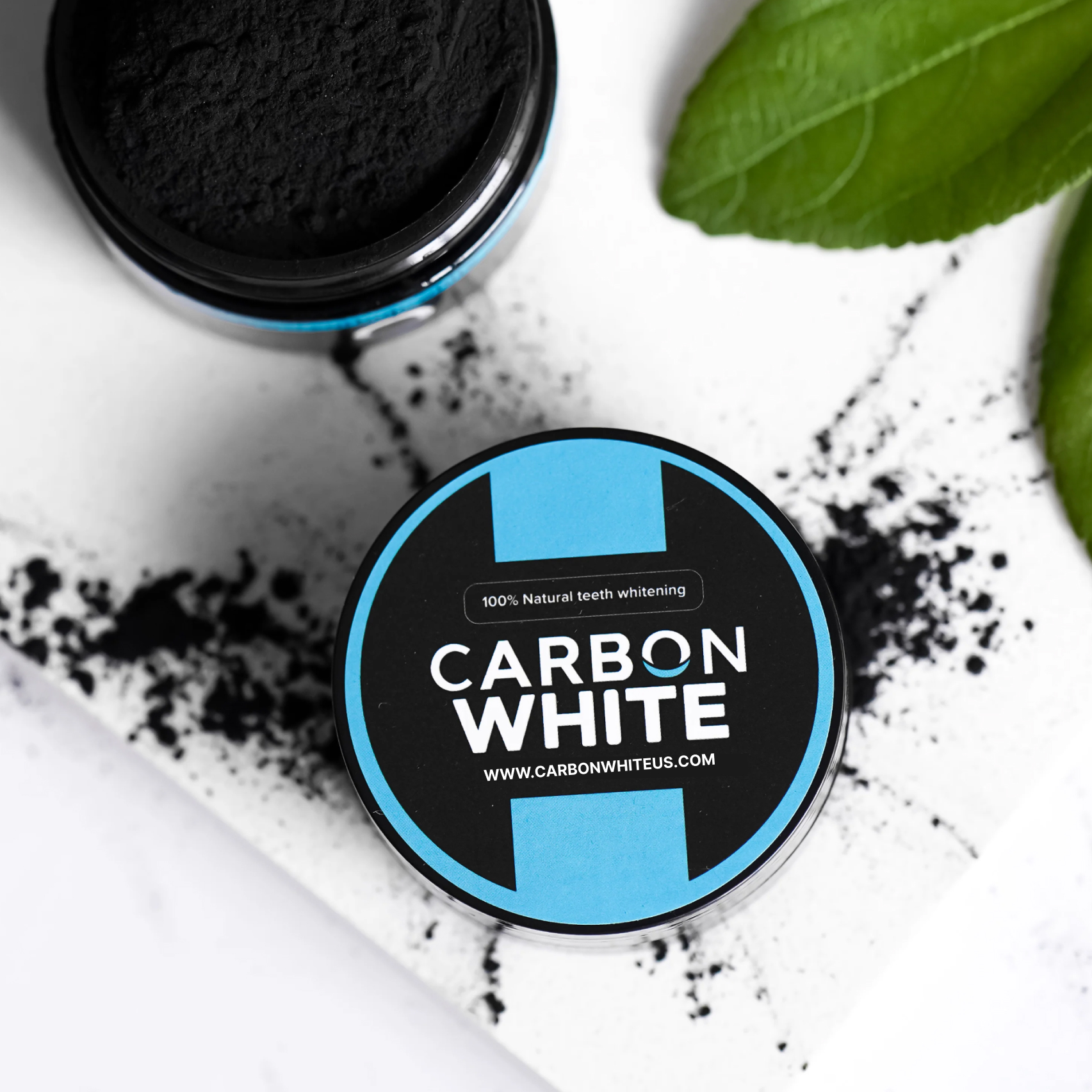 Carbon White teeth whitening powder with black powder spill and green leaves.