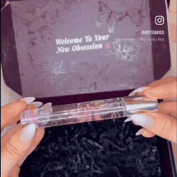 Hands holding a perfume bottle in front of a decorative box.