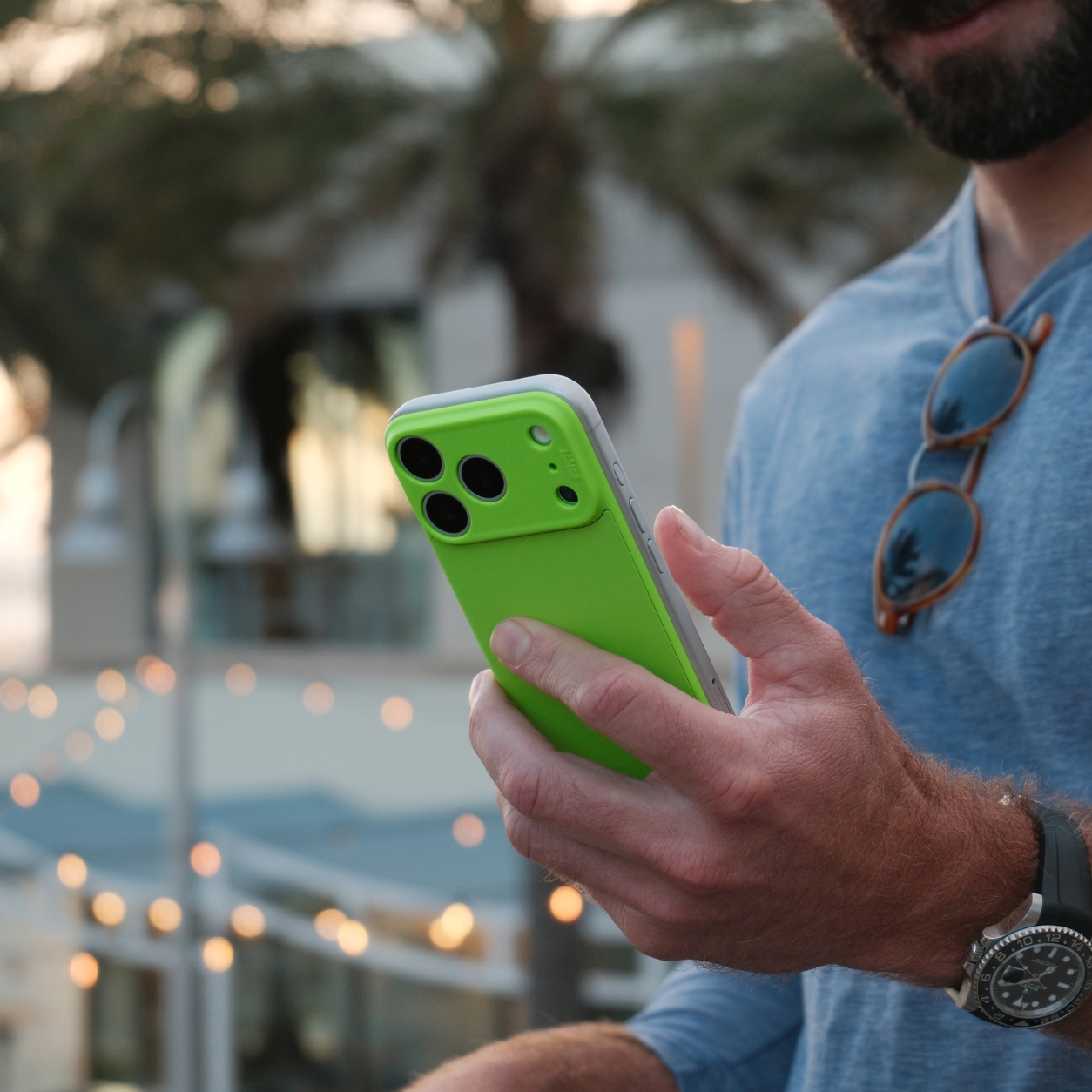 A man in a blue shirt holds a smartphone in a bright green case.