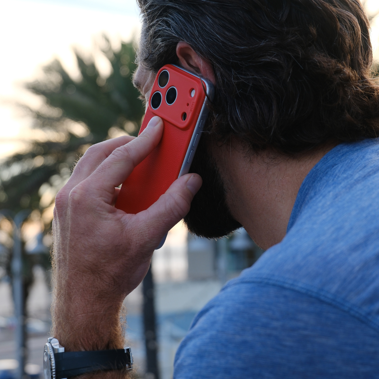 A man viewed from behind, holding a smartphone in a red case to his ear.