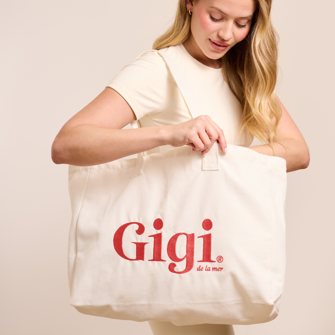A woman looks into a cream-colored canvas tote bag with the red logo 'Gigi de la mer'.
