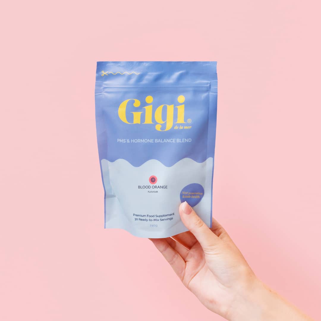 Hand holding a Gigi PMS & Hormone Balance Blend bag against a pink background.