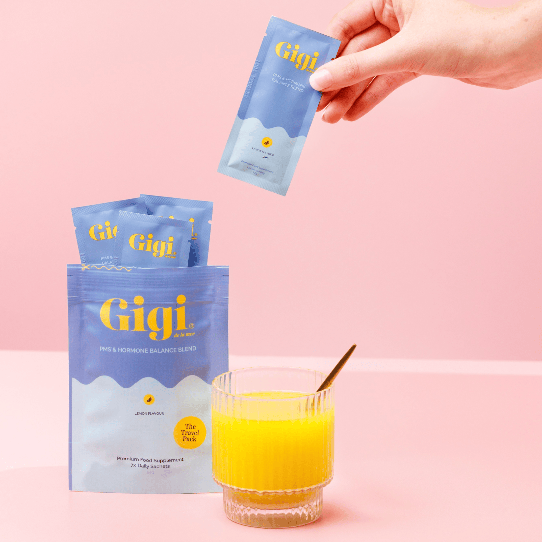 Drink mix packet being poured into a glass with Gigi PMS supplement packaging and lemon slices.