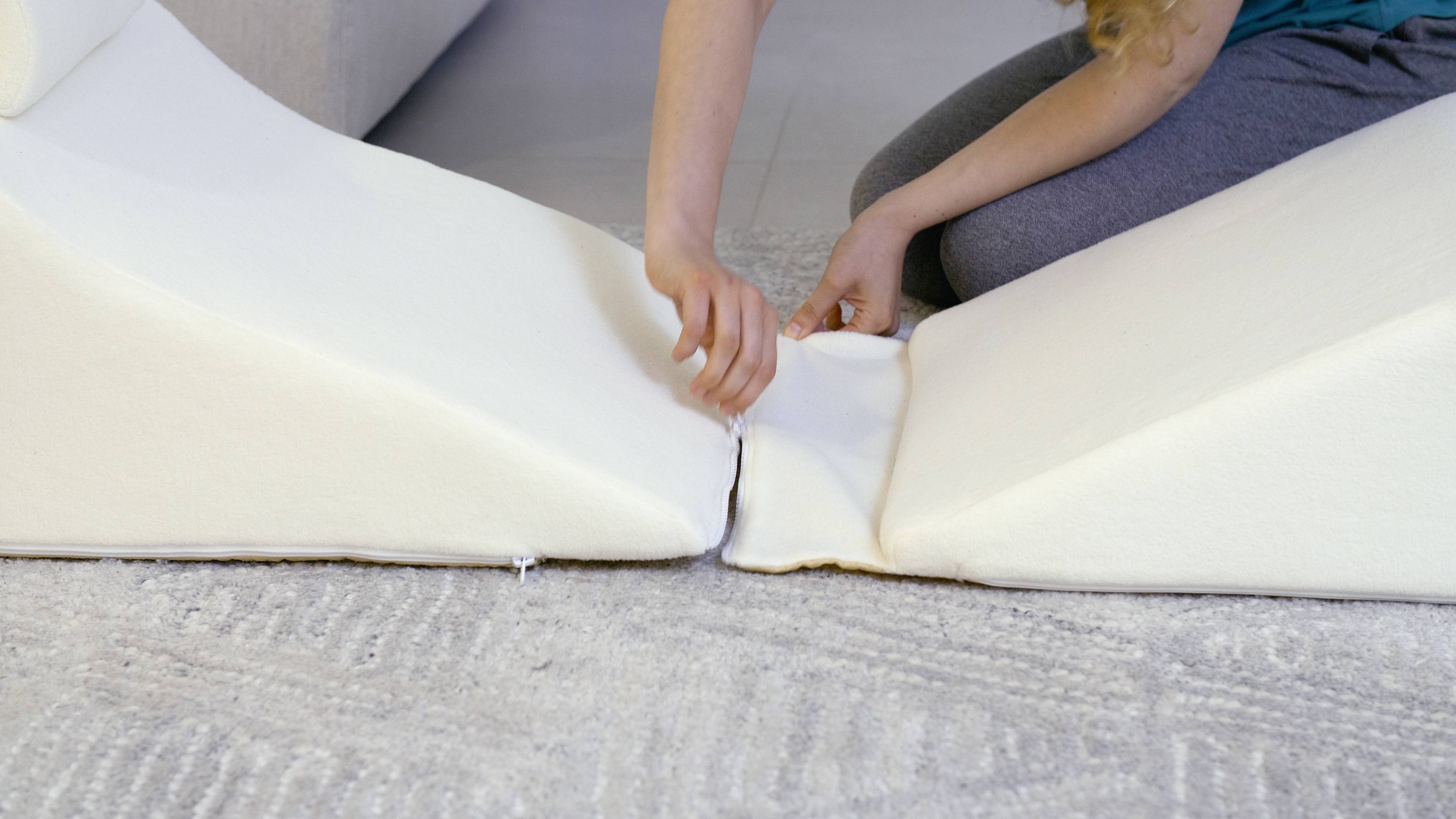 Person zipping two white foam cushions together on a carpet.