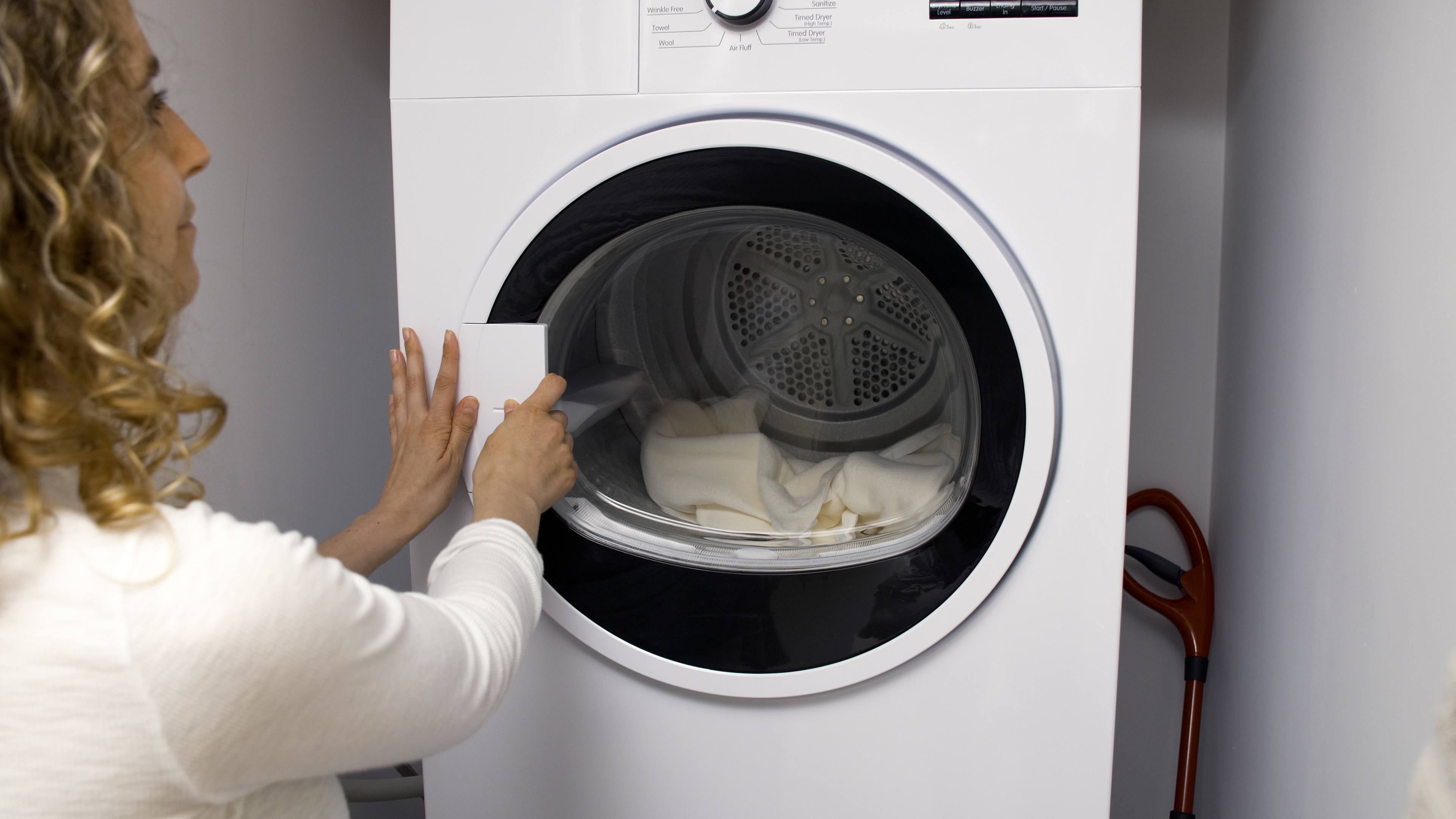Person opening a front-loading washing machine with clothes inside.