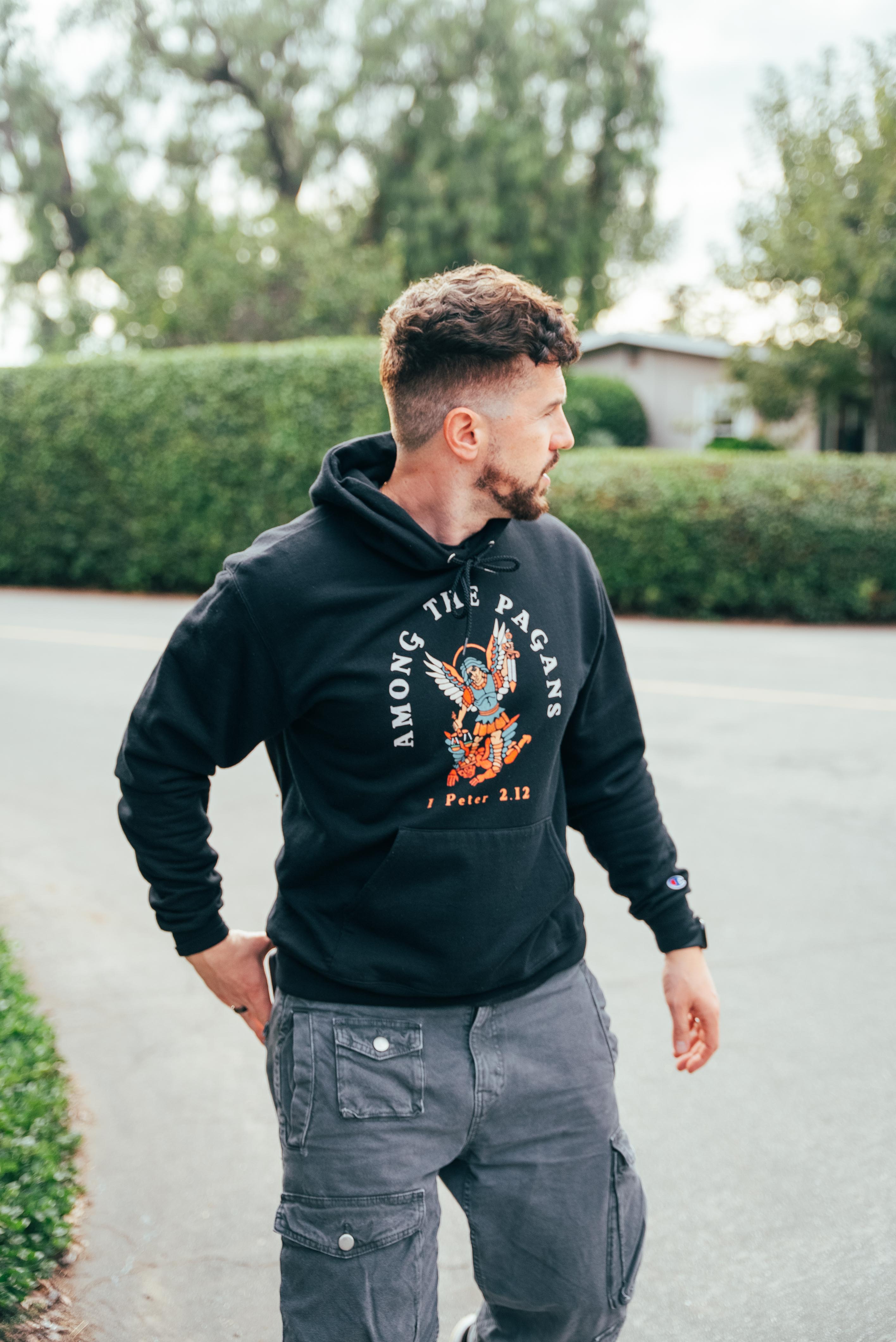 Man in a black hoodie stands outdoors, looking to the side.