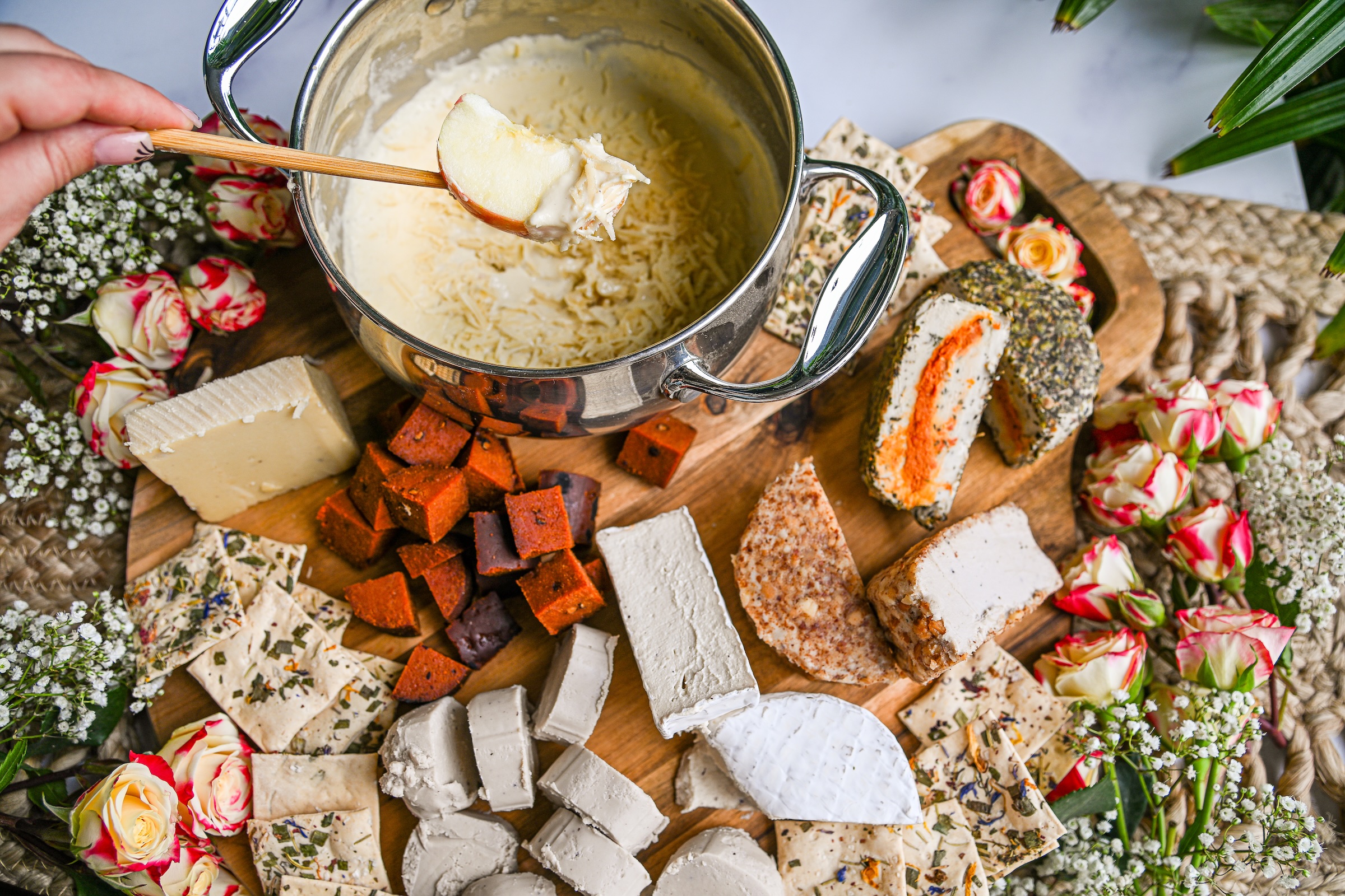 An overhead view of a hand dipping an apple slice into a pot of cheese fondue on a board.