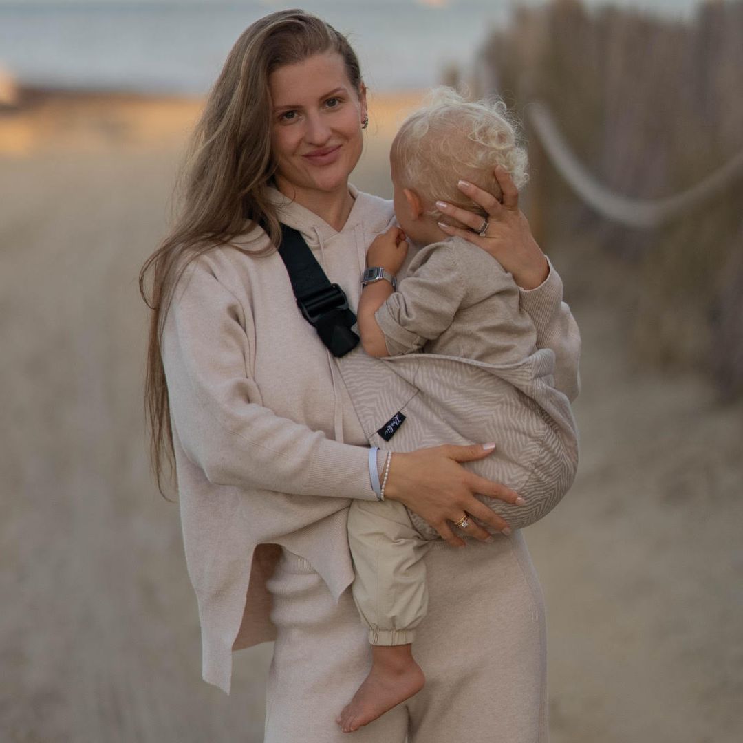 Woman holding a child in a sandy outdoor setting.