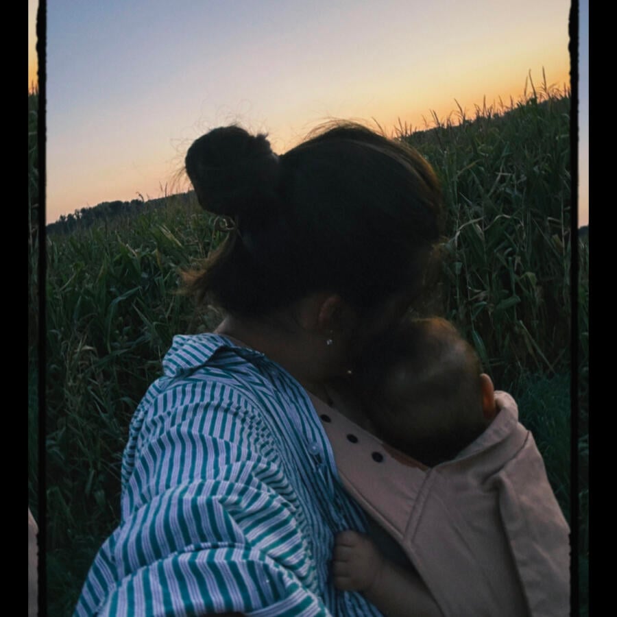 Person holding a baby in a field at sunset.
