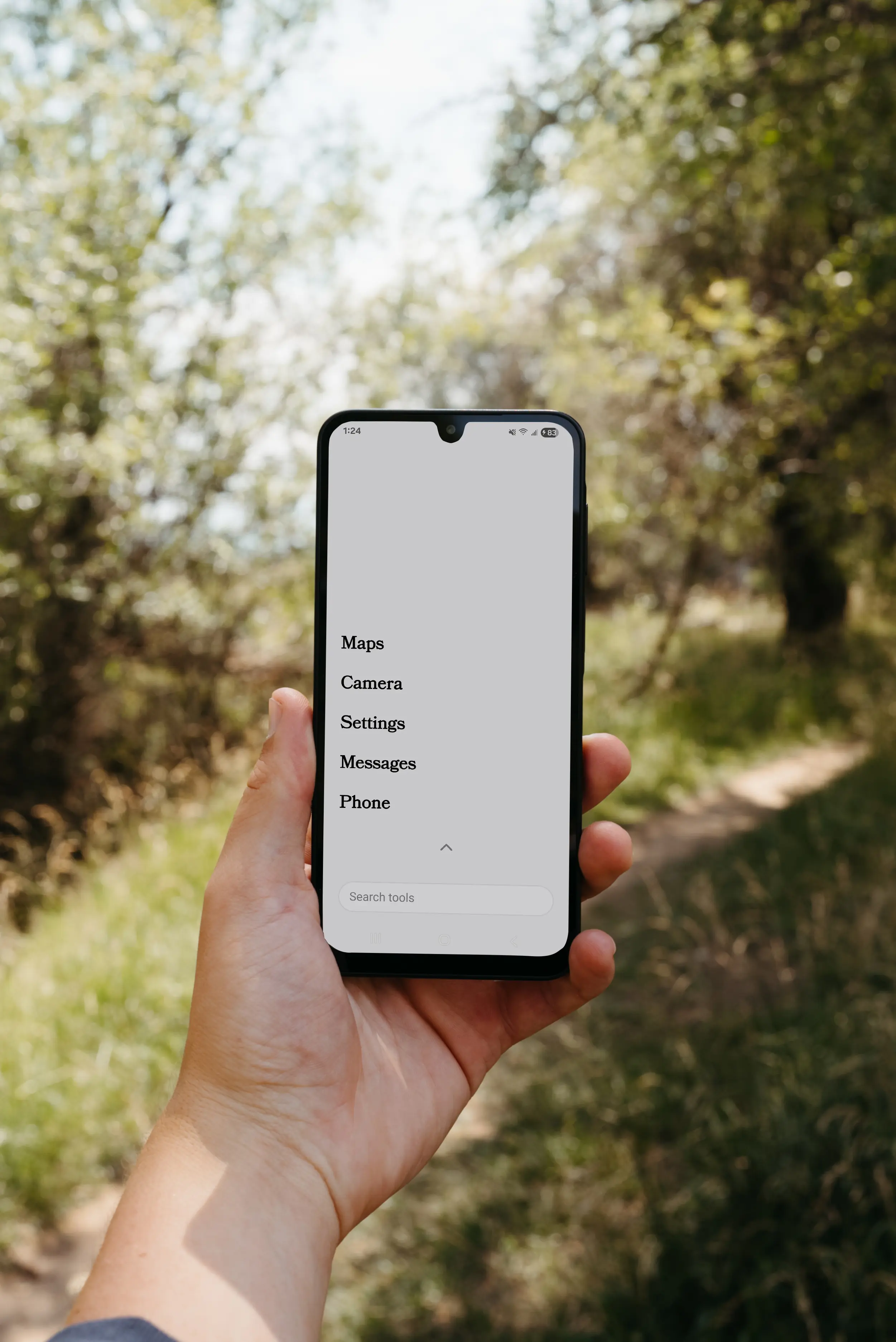 A person's hand holding a smartphone outdoors, displaying a minimalist app menu on a white screen.