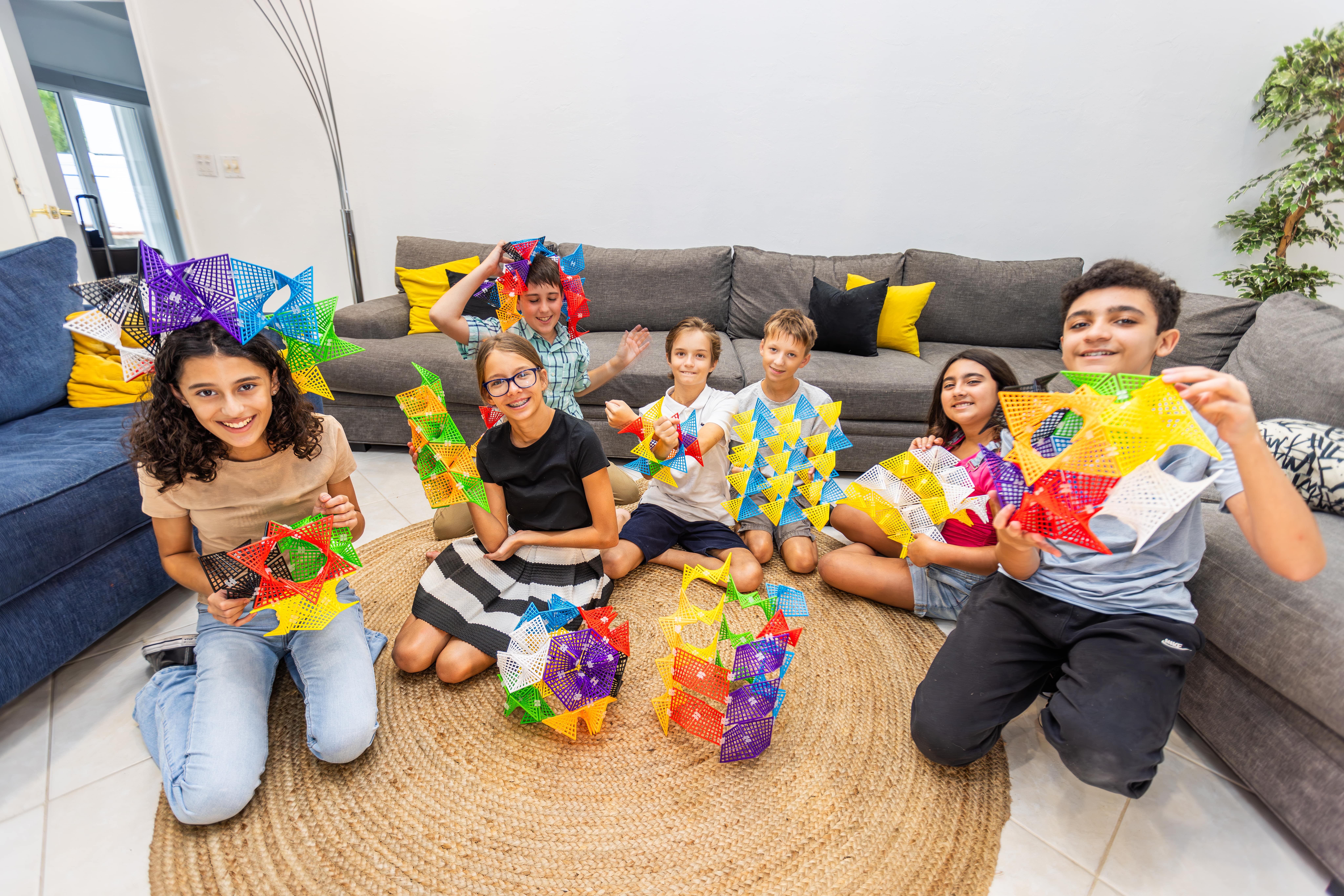 Children sitting on a rug holding colorful geometric shapes indoors.
