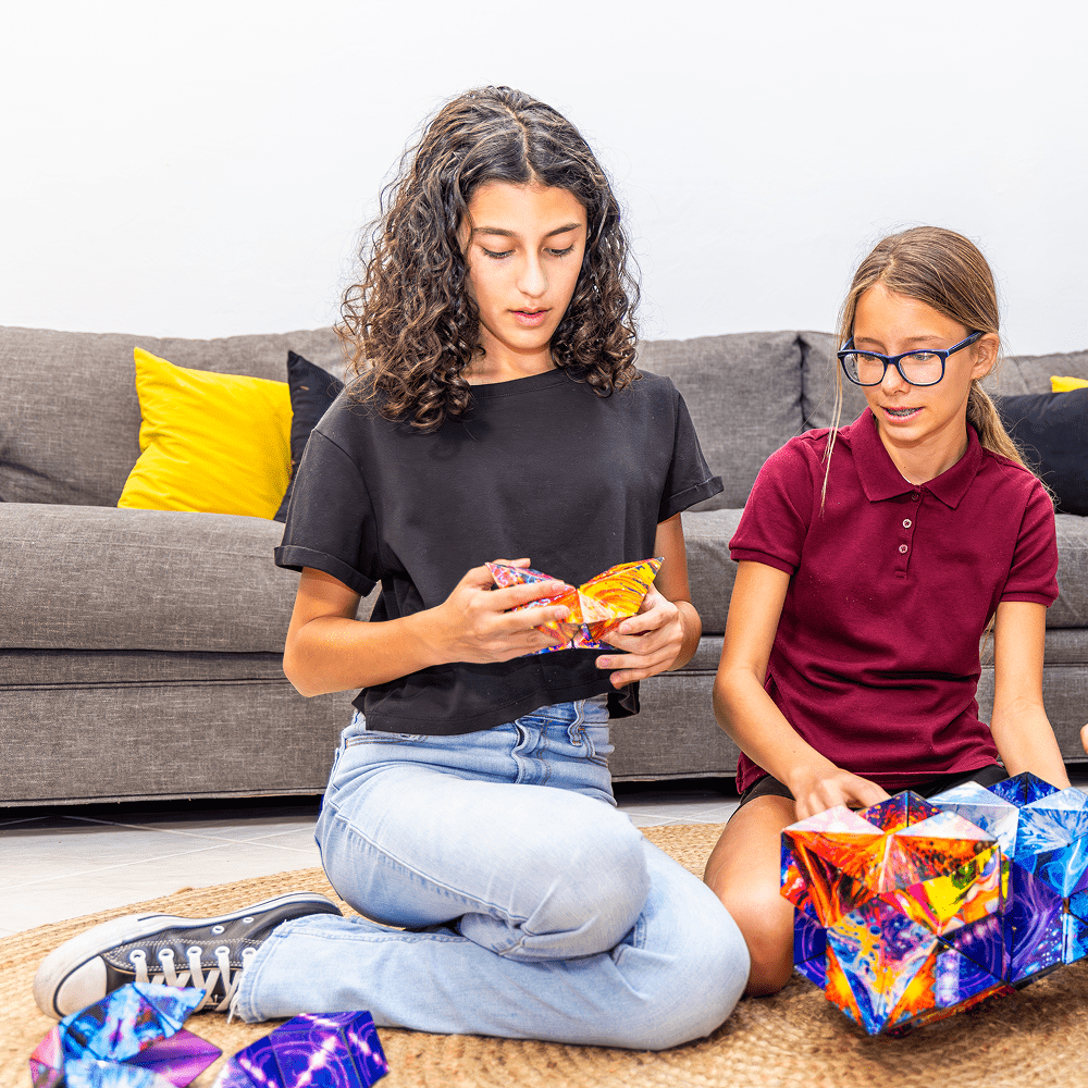 Two children sitting on the floor assembling colorful geometric shapes.