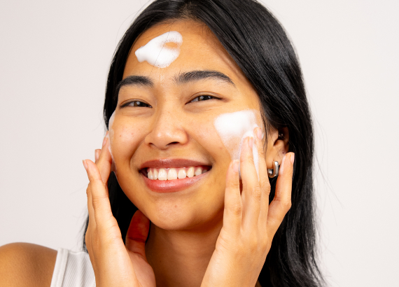Smiling person applying facial foam on face and forehead.