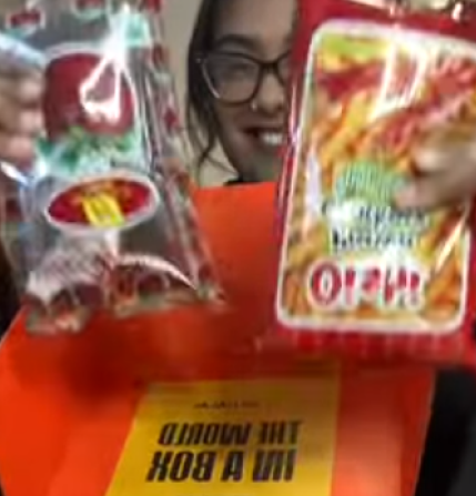 Person holding two snack packages in front of an orange box.