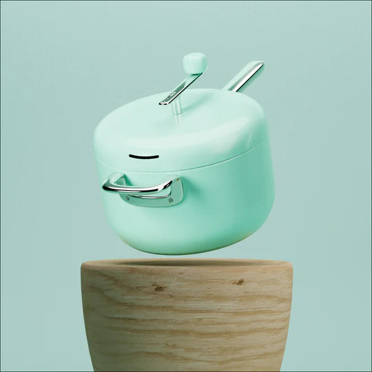 A mint green pot with a crank on its lid floating above a wooden base against a green background.