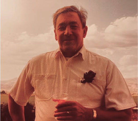 Man in a white shirt holding a drink outdoors with a cloudy sky.