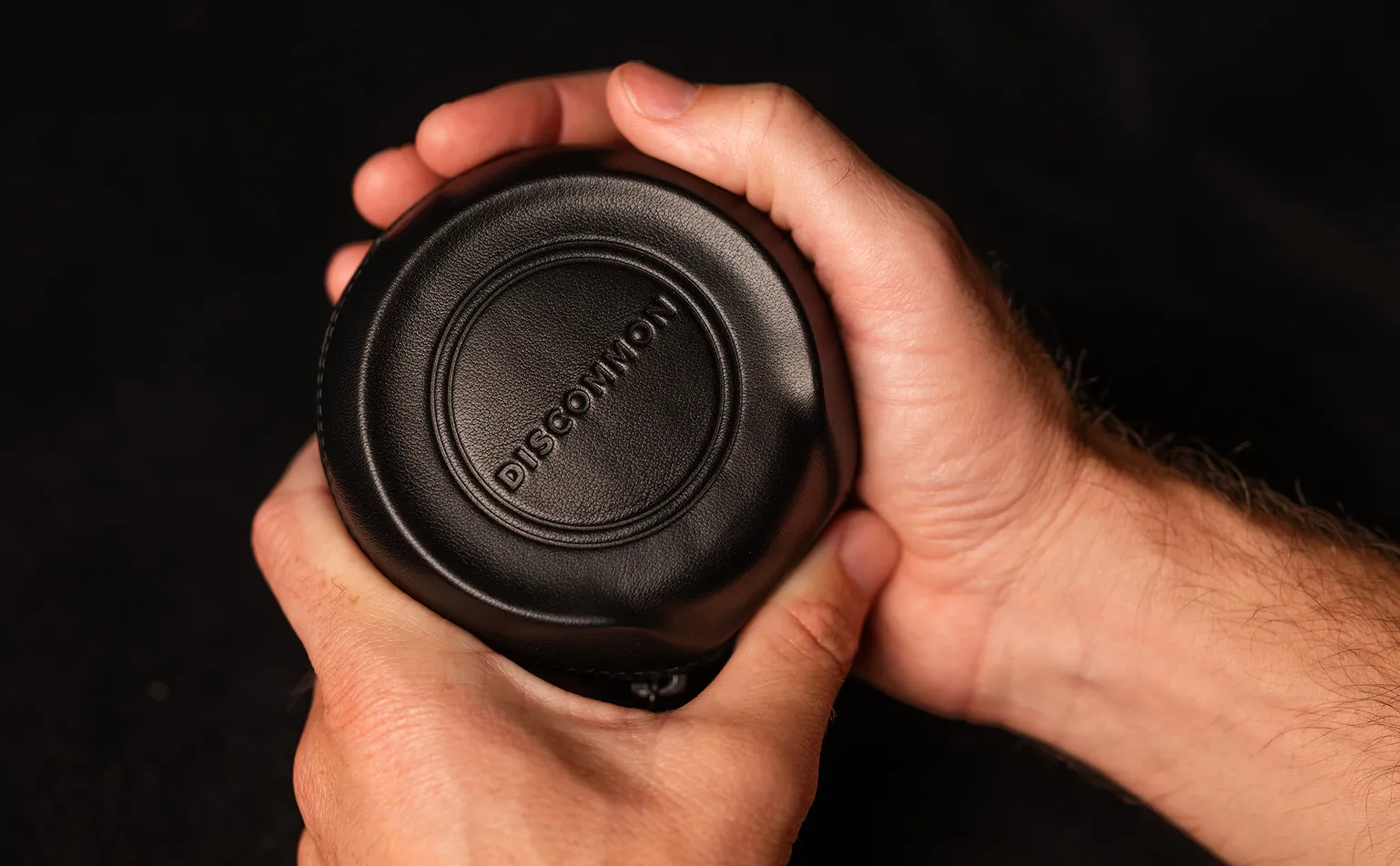 A person's hands holding a round, black leather object with the word Discommon embossed on top.