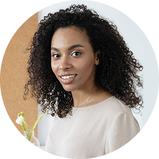 Person with curly hair smiling in front of a corkboard.