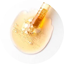 A close-up of a glass dropper dispensing a bubbly, golden-yellow liquid onto a white surface.