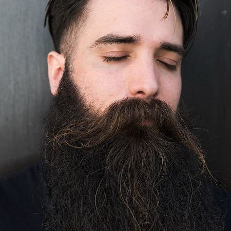 Man with a long beard and closed eyes against a dark background.