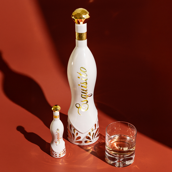 Two elegant bottles and a glass on a red surface.