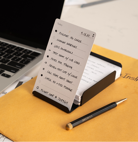 A to-do list on a stand next to a laptop and pencil.