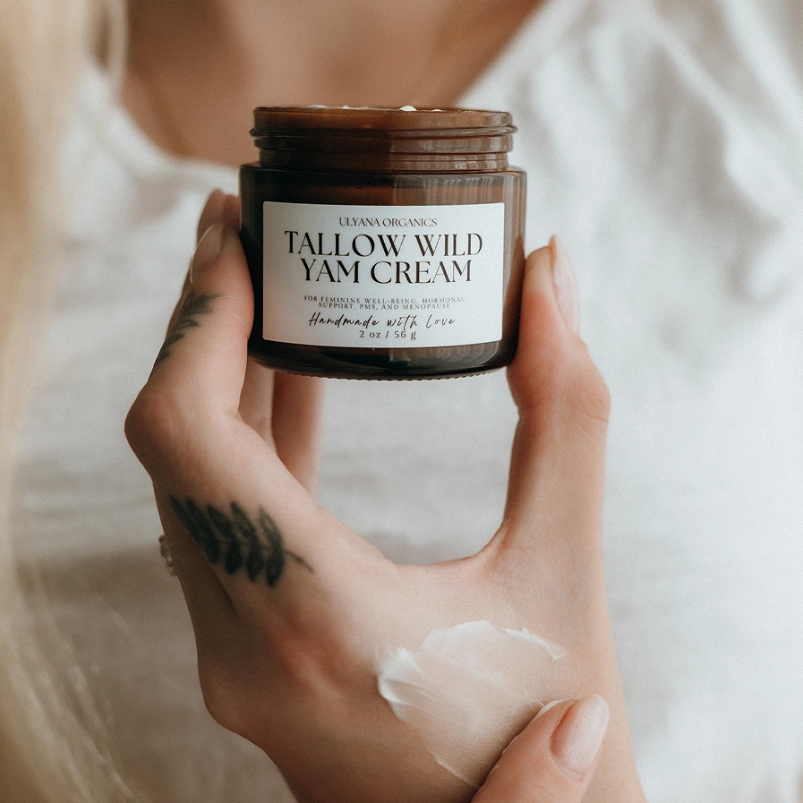 Person holding a jar of Tallow Wild Yam Cream with visible tattoos.