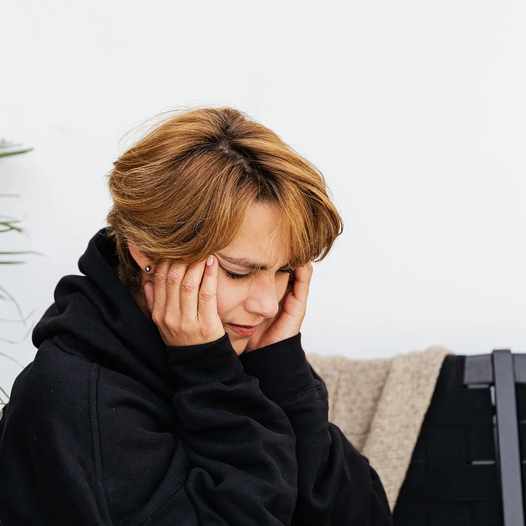 A person in a black hoodie holds their hands to their temples with their eyes closed.