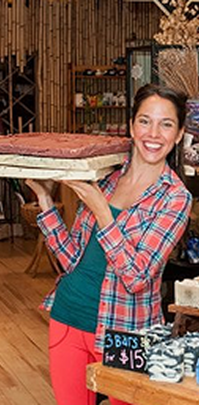 Person in blue apron showing racks of colorful soap bars.