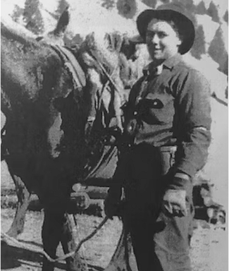Person in outdoor attire standing beside a horse in a mountainous area.