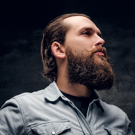 Man with a beard and long hair, wearing a light blue shirt, looking to the side.