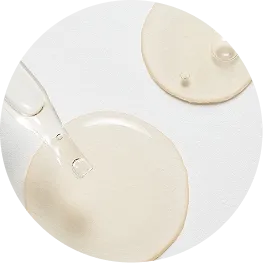 A close-up of a clear dropper dispensing a light-colored liquid serum onto a white surface.