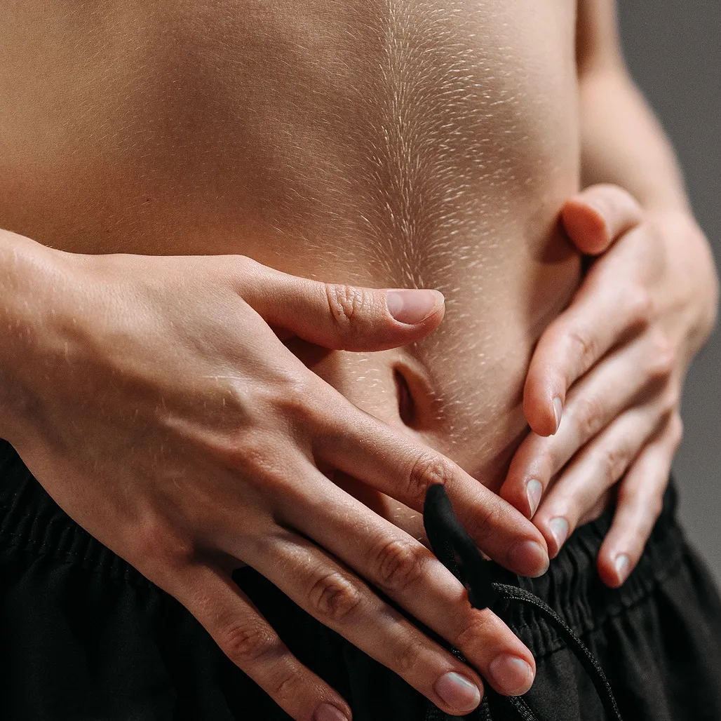 A close-up of a person's hands resting on their bare abdomen.
