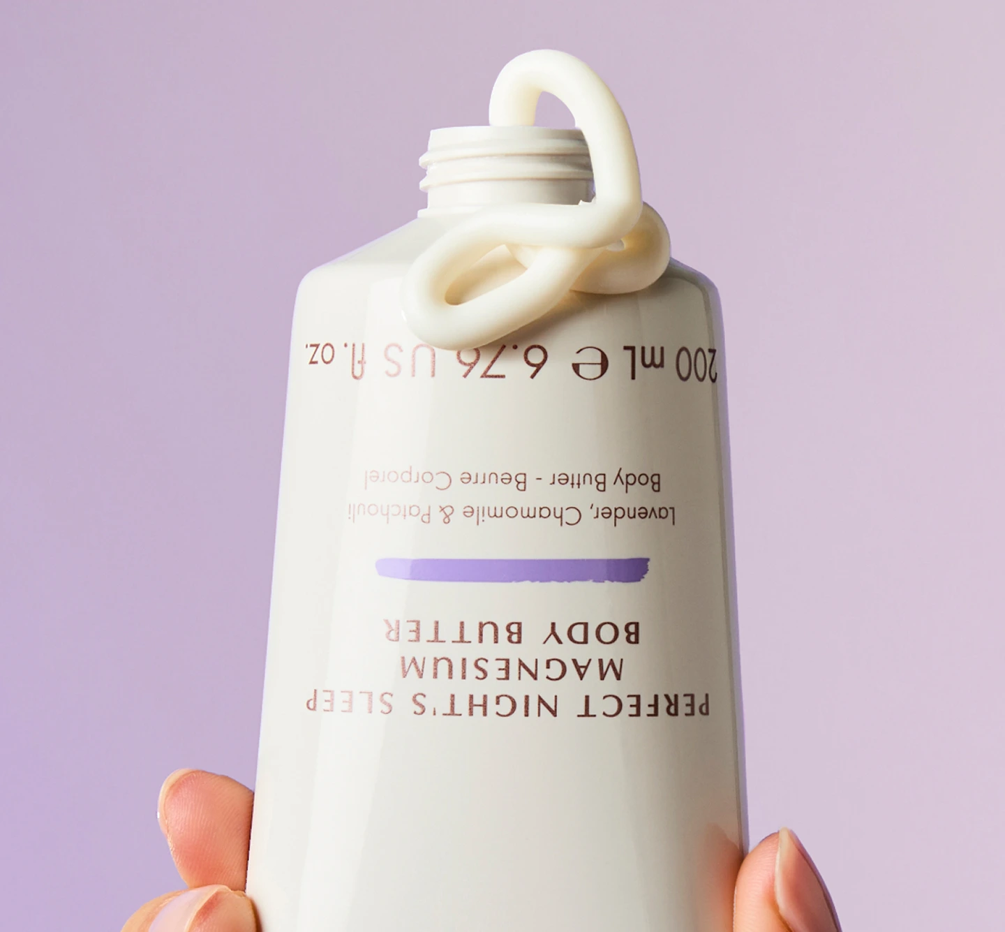 A hand holds a white tube of body butter with cream squeezed out onto the top.
