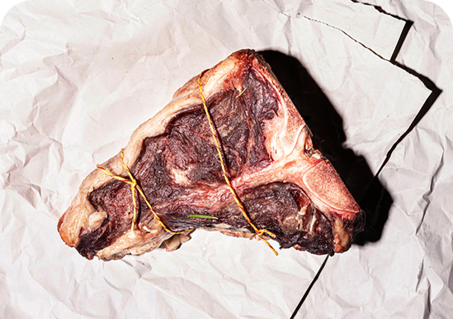 Raw T-bone steak tied with string on crumpled paper.