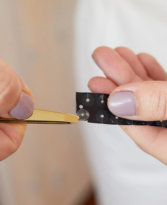 Hands holding tweezers and a strip with small circular objects.