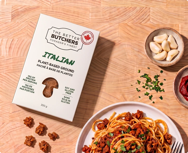 A box of The Better Butchers plant-based ground next to a plate of spaghetti and ingredients on a wood surface.