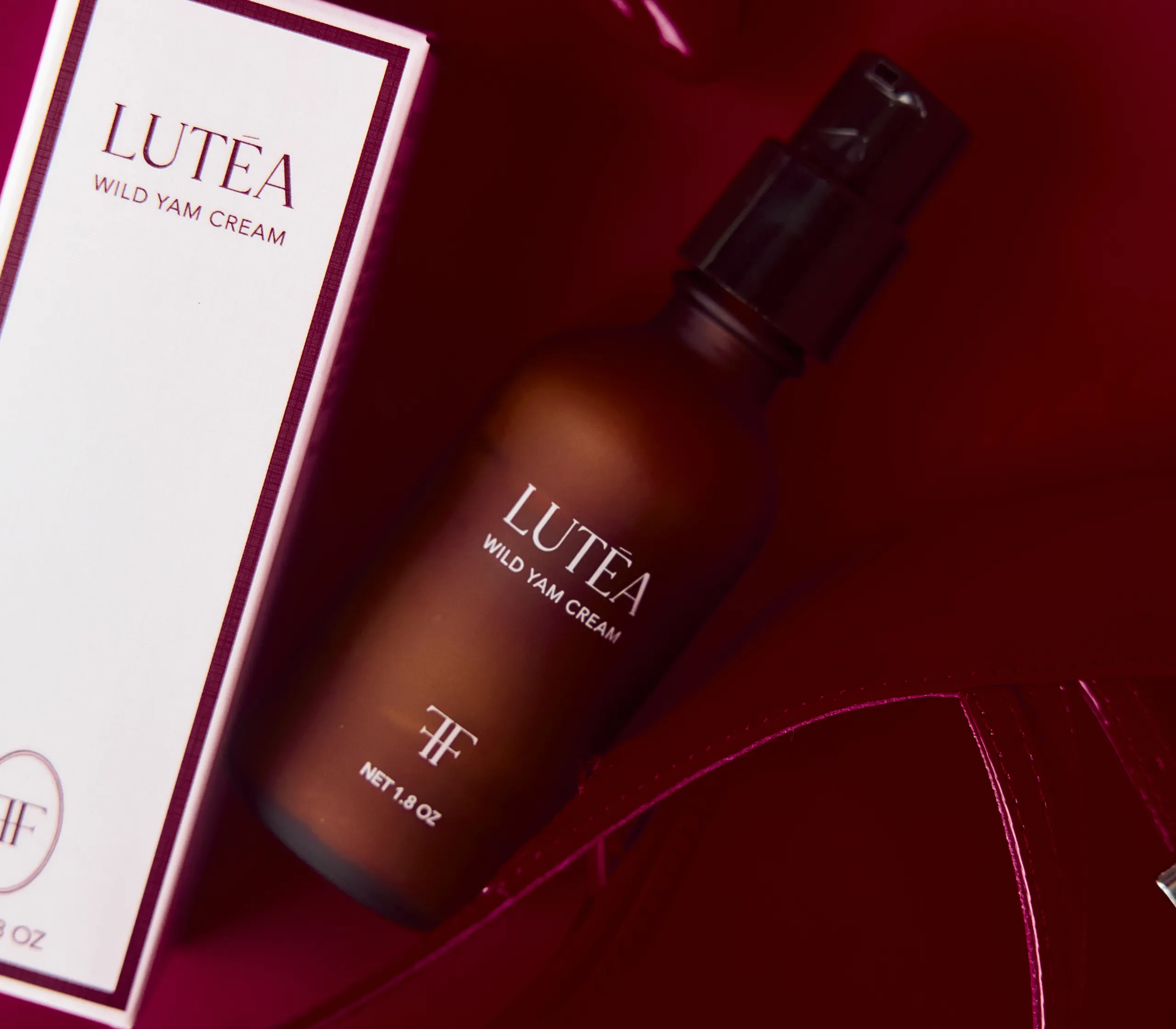 A bottle and box of Lutea Wild Yam Cream sitting on a glossy, dark red surface.