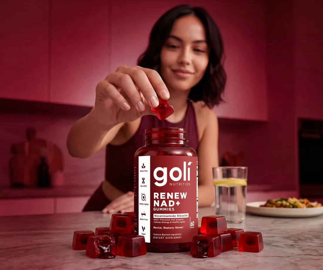 A woman takes a red gummy from a bottle of Goli Renew NAD+ Gummies on a counter.
