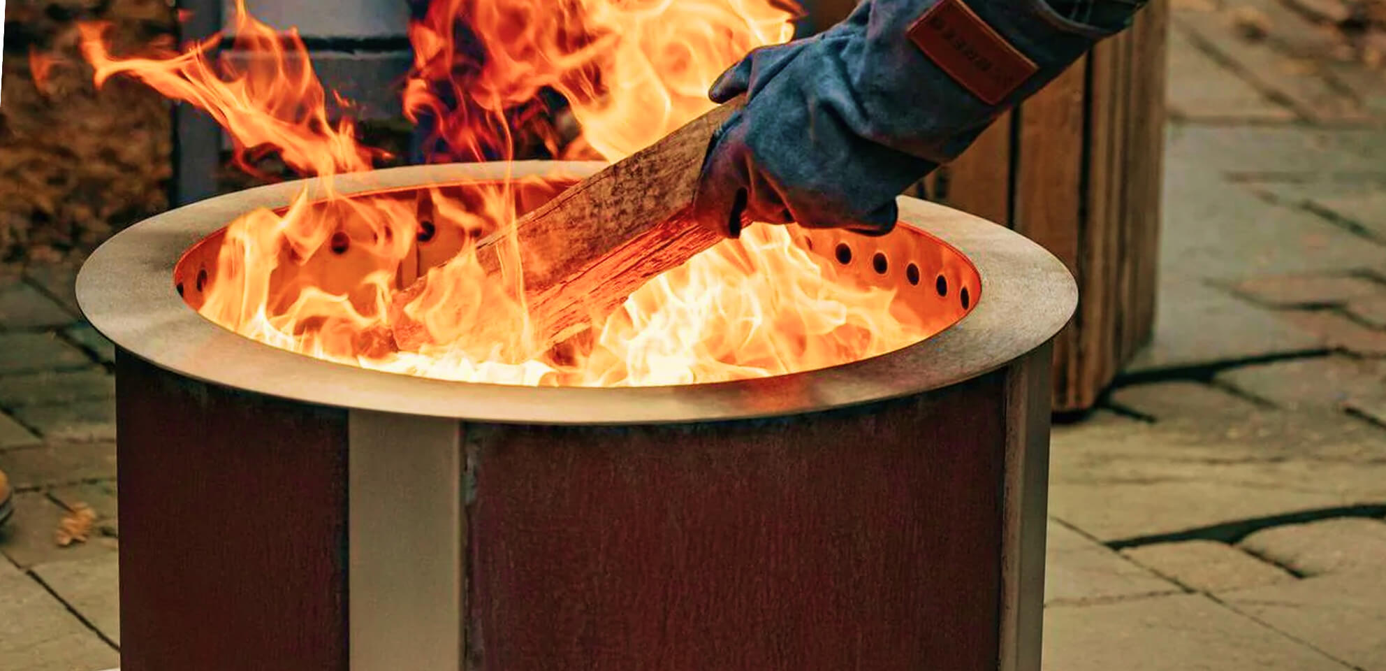 Person adding wood to a fire pit with flames.