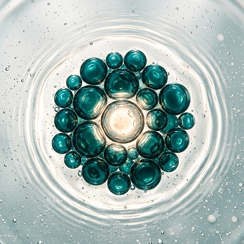 A central clear bubble is surrounded by a cluster of smaller teal-colored bubbles in a clear liquid.