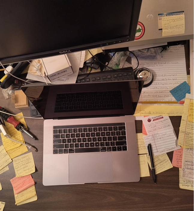 Cluttered desk with a laptop, sticky notes, and papers.