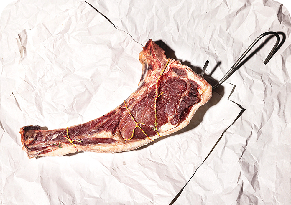 Raw tomahawk steak on crumpled white paper with a metal hook.