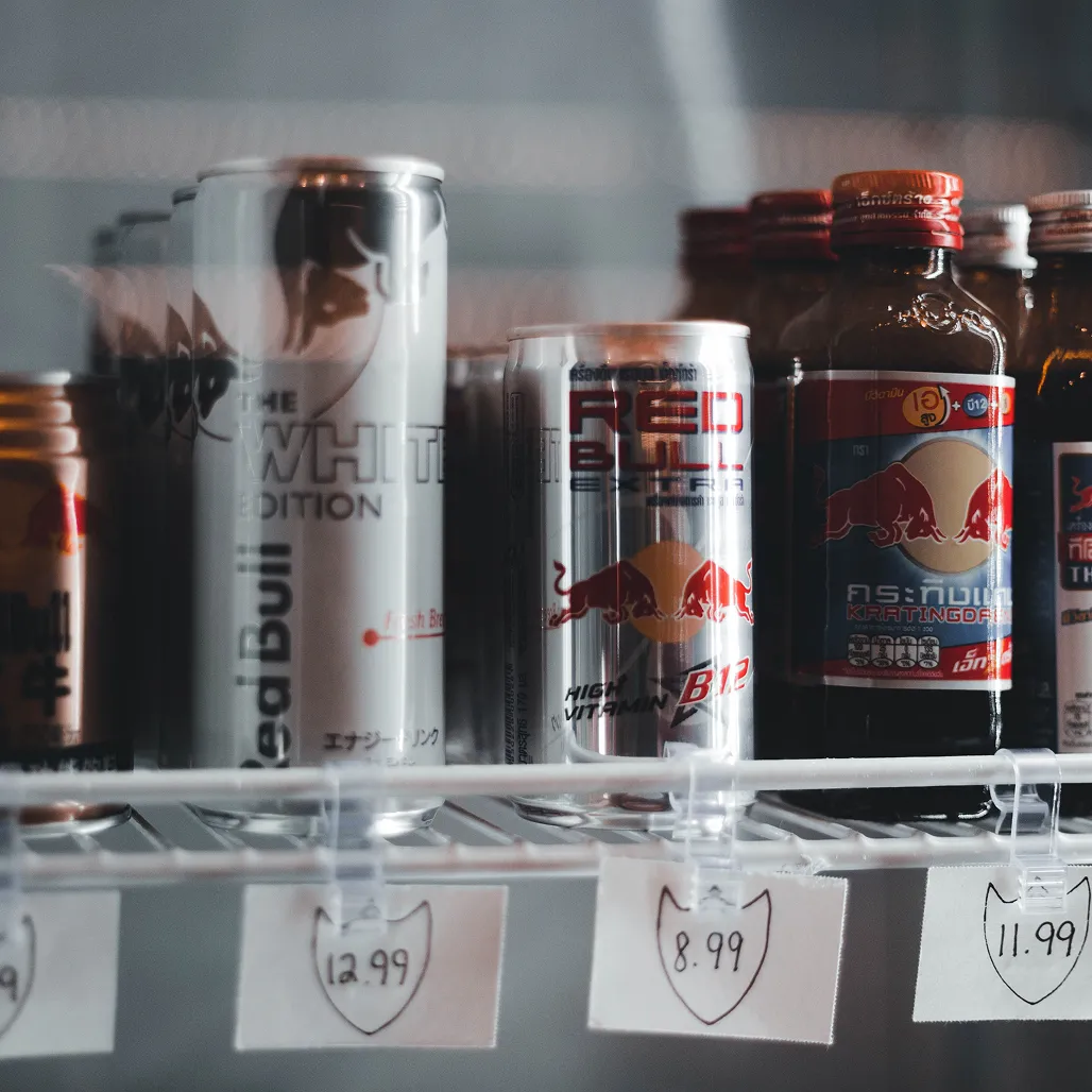Various Red Bull energy drinks and Krating Daeng bottles on a refrigerated shelf with price tags.